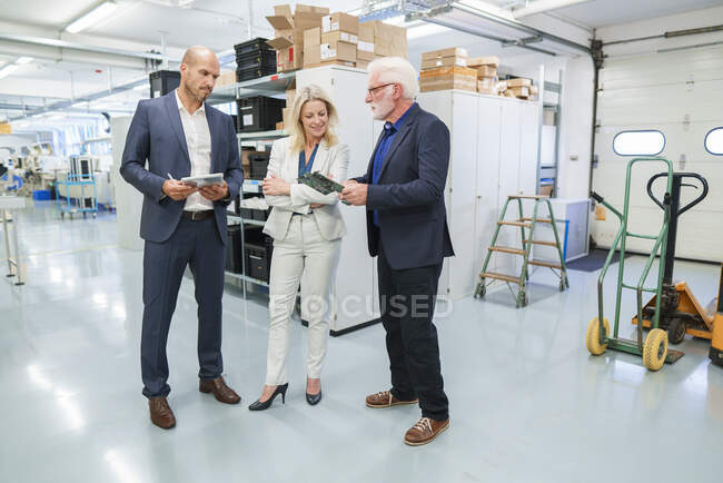 Senior businessman discussing over machine part with colleagues at illuminated industry — Stock Photo