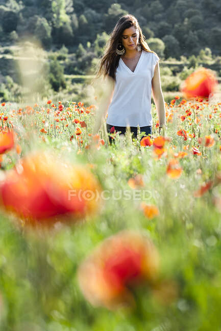 Jovem mulher em pé no meio de plantas de papoula no campo durante a primavera — Fotografia de Stock