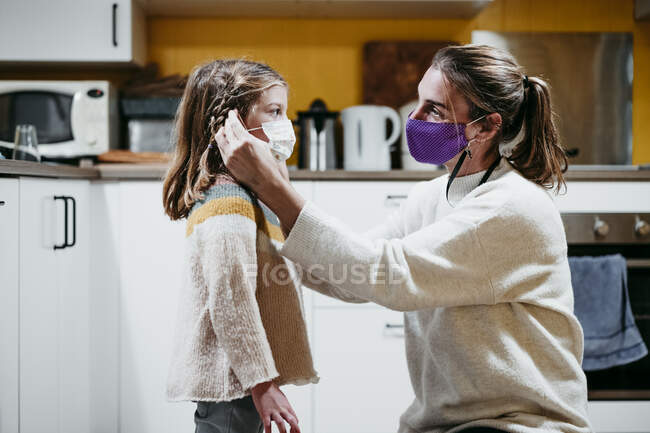 Мама підлаштовує маску обличчя дочки, сидячи вдома. — стокове фото