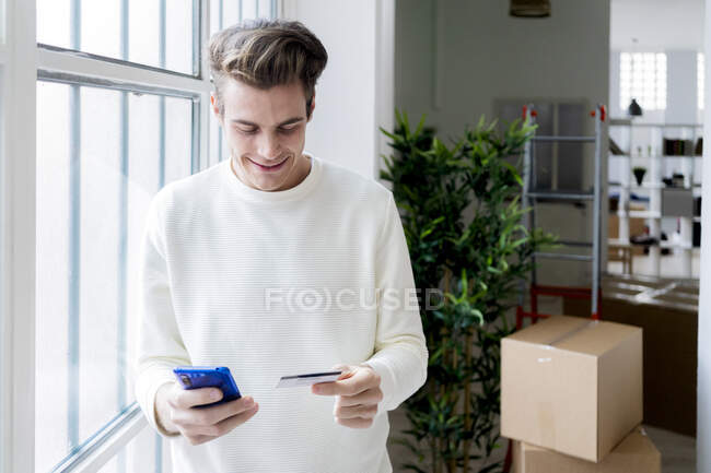 Smiling man paying by credit card through smart phone in new loft apartment — Stock Photo