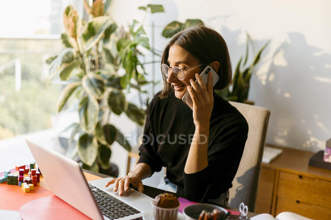 Metà donna d'affari adulta parlando su smart phone mentre si utilizza il computer portatile seduto a casa — Foto stock