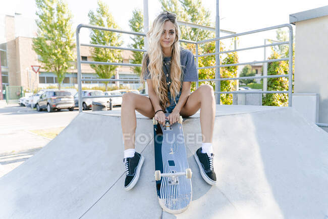 Прекрасна блондинка сидить з скейтбордом на атракціоні в парку. — стокове фото