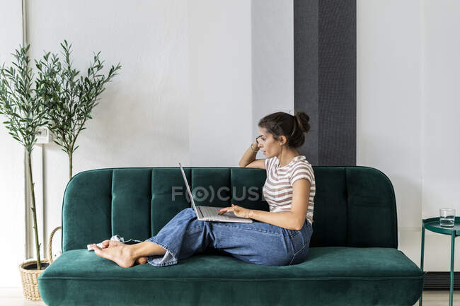 Profesional de diseño femenino seguro usando el ordenador portátil mientras está sentado en el sofá en la oficina creativa - foto de stock