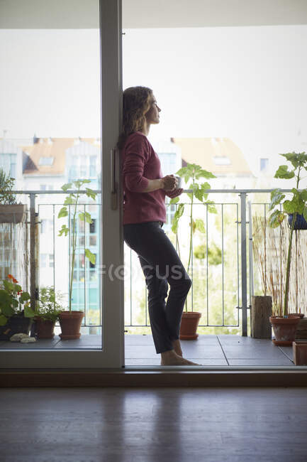 Femme buvant du café tout en restant près du balcon à la maison — Photo de stock