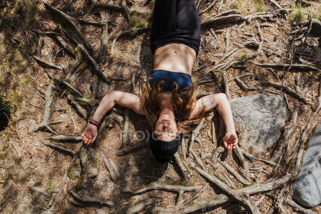 Mujer despreocupada relajándose en un terreno cubierto de raíces en el bosque en La Pedriza, Madrid, España - foto de stock