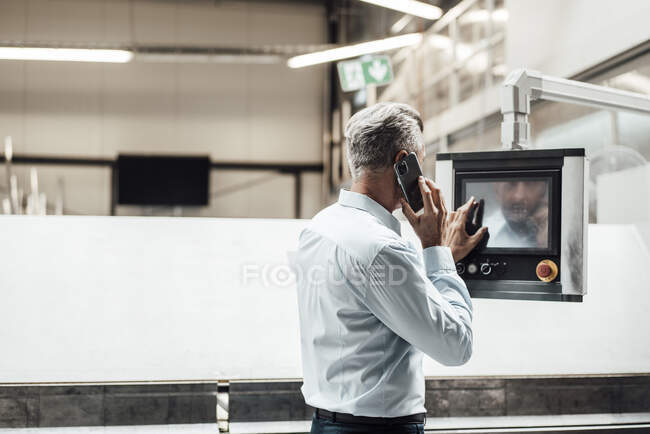 Male engineer talking on smart phone while operating equipment in industry — Stock Photo