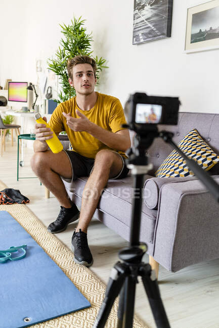 Treinador de fitness gravação sessão de fitness na câmera enquanto sentado no sofá em casa — Fotografia de Stock