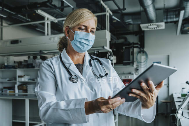 Scientist wearing face mask using digital tablet while standing at laboratory — Stock Photo