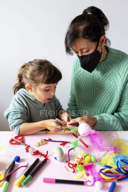 Grandmother and granddaughter making creative toys from pipe cleaners and pom-pom at home during pandemic — Fotografia de Stock