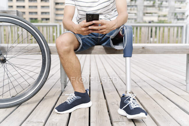 Section basse de l'homme avec un membre artificiel en utilisant le téléphone mobile en ville — Photo de stock