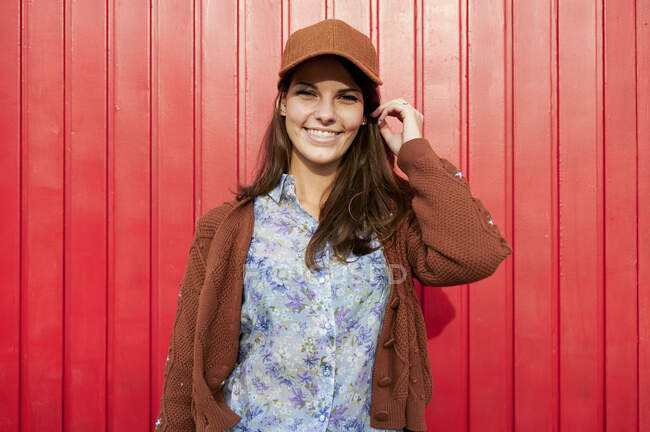 Улыбающаяся женщина в шляпе, стоящая напротив красной металлической двери — стоковое фото