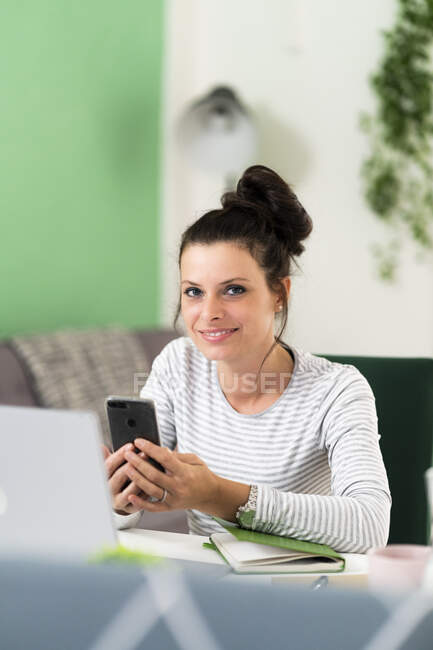 Жінка користується розумним телефоном, сидячи вдома на стільці. — стокове фото