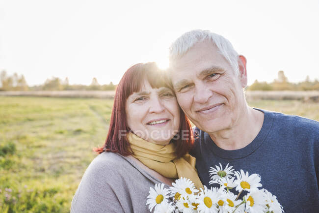 Smiling senior couple with chamomile flowers — Stock Photo