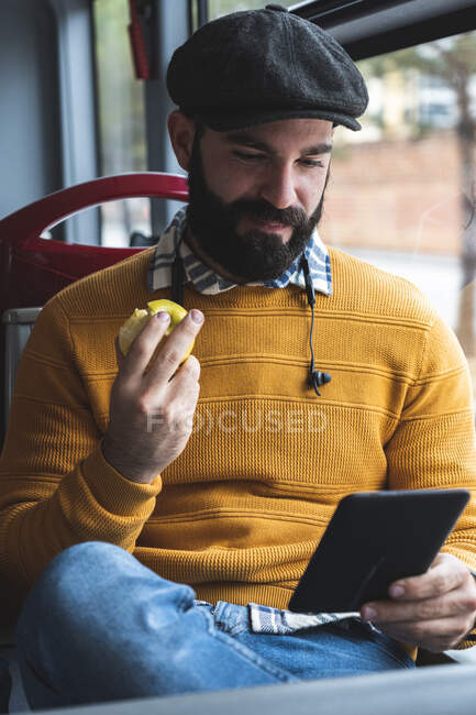 Uomo d'affari sorridente utilizzando tablet digitale pur avendo frutta in autobus — Foto stock