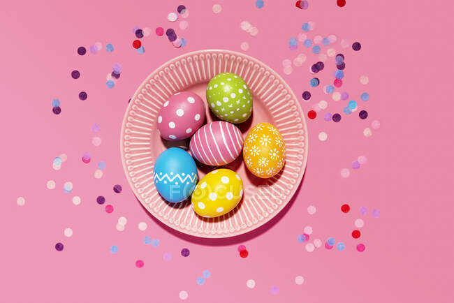 Colorful hand colored Easter eggs in tray with confetti on pink background — Stock Photo