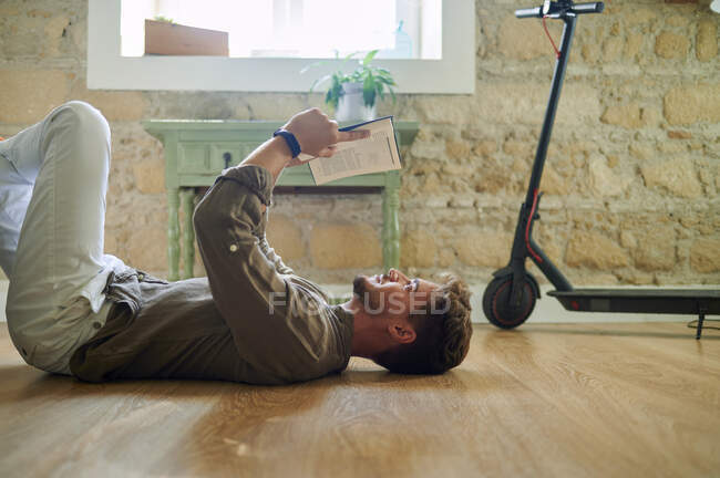 Kaukasischer Mann liegt auf dem Boden, während er im Wohnzimmer Buch liest — Stockfoto