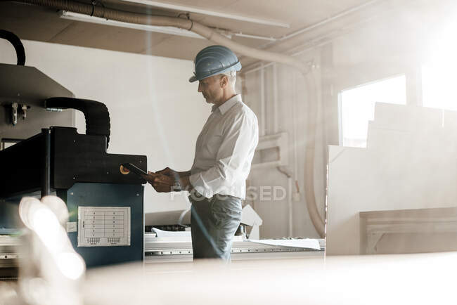 Engenheiro usando tablet digital em pé por equipamentos de fabricação na fábrica — Fotografia de Stock