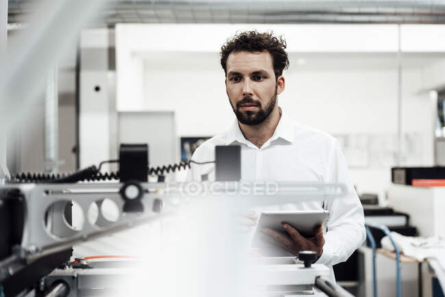 Hombre profesional mirando maquinaria mientras sostiene tableta digital en la industria — Stock Photo
