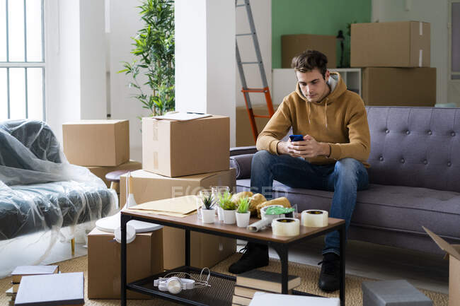 Young man using smart phone while moving in new loft apartment — Stock Photo