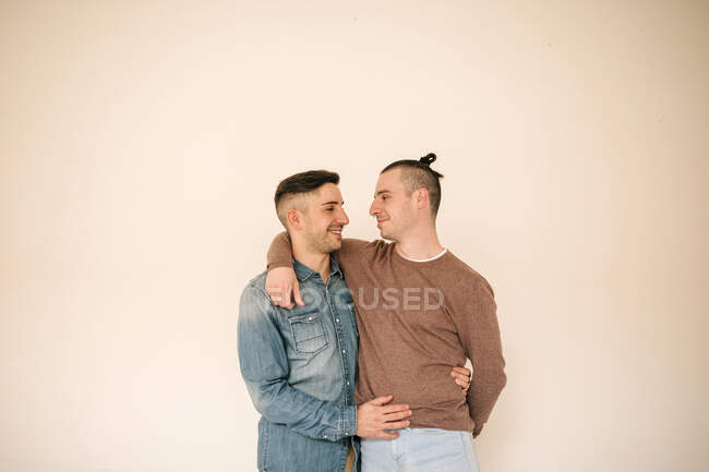 Happy gay couple with arm around standing against beige background — Stock Photo