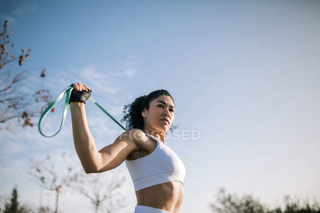 Sportswoman looking away while stretching resistance ban against sky — Foto stock