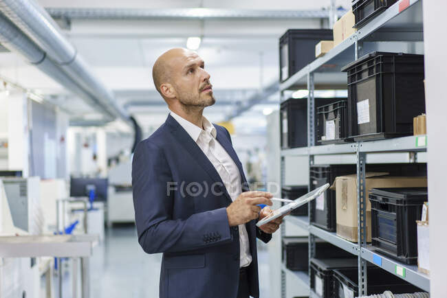 Зрілий чоловік з цифровим планшетом, який дивиться на контейнери на стійці в промисловості. — стокове фото