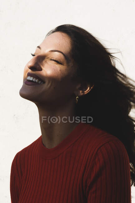 Young brunette woman laughing against wall on sunny day — Stock Photo