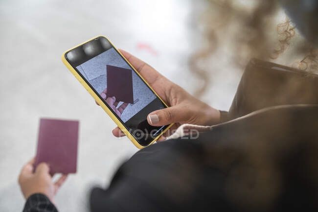 Mujer tomando una foto del pasaporte en el teléfono inteligente mientras está de pie en el aeropuerto - foto de stock