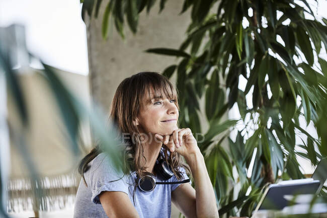 Thoughtful woman smiling while sitting with head in hands at home — Stock Photo