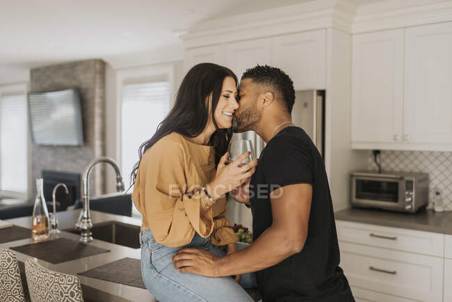 Мужчина целует женщину, сидя дома на кухонном столе — стоковое фото