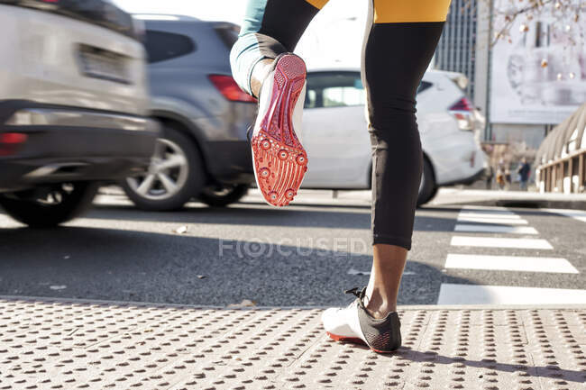 Mujer joven con zapato deportivo cruzando la carretera en el tráfico mientras corre en la ciudad - foto de stock