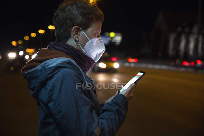 Femme avec masque protecteur utilisant un téléphone portable tout en étant debout en ville — Photo de stock