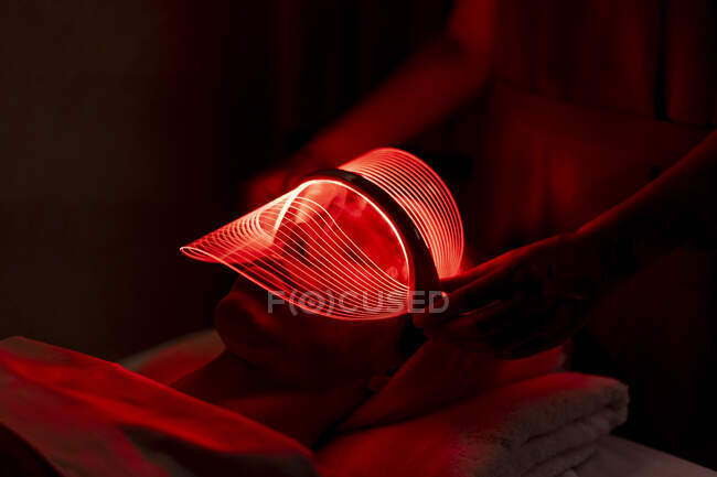 Mujer joven con máscara roja durante el tratamiento rejuvenecedor en el spa de belleza - foto de stock