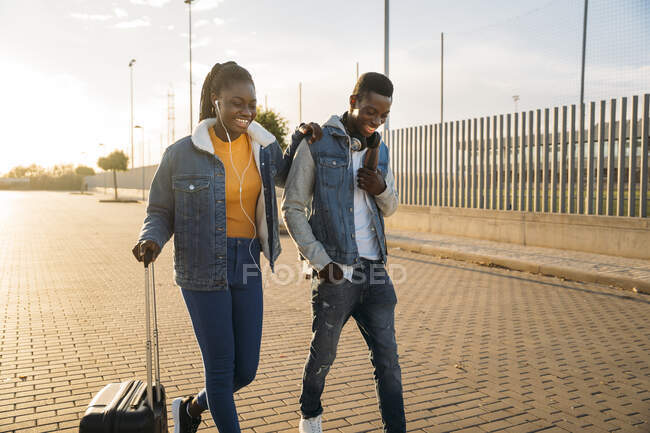 Glückliche Freundin mit Rollgepäck spaziert mit Freund auf Straße — Stockfoto