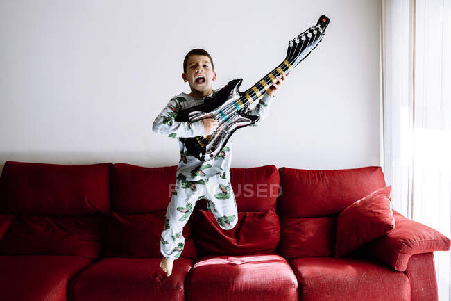Хлопчик стрибає з дивана під час гри на гітарі у вітальні. — стокове фото