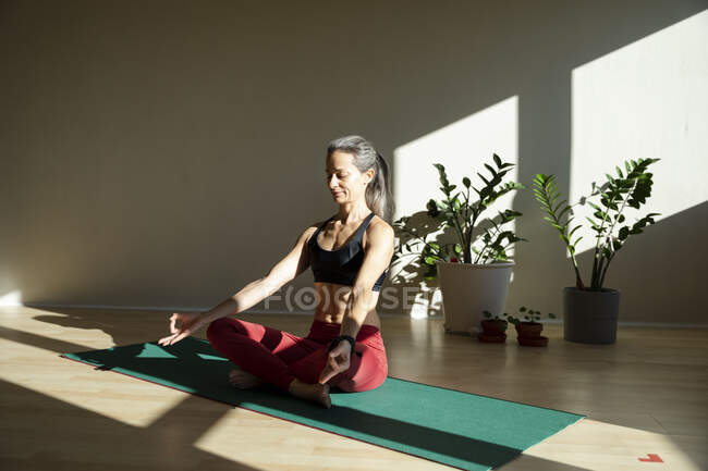 Yogini medita sul tappetino da ginnastica in salotto nella giornata di sole — Foto stock