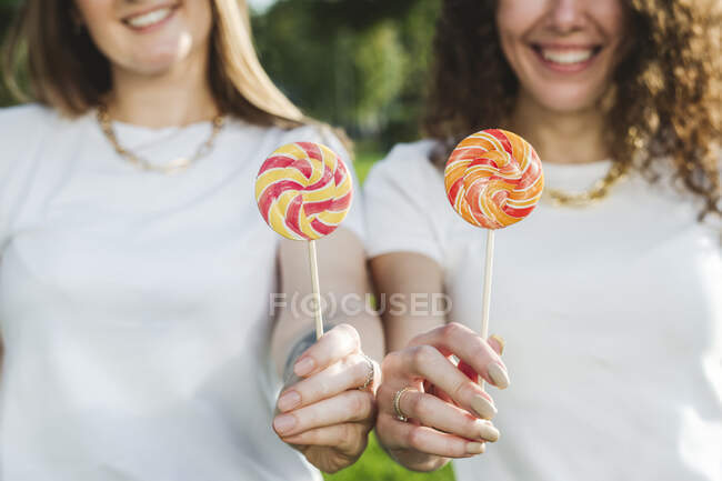 Smiling women holding lollipops at park on sunny day — Stock Photo