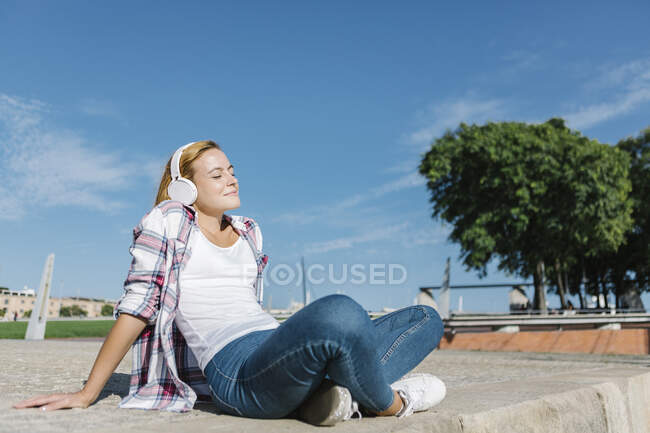 Donna che ascolta musica mentre siede sul sentiero durante la giornata di sole — Foto stock