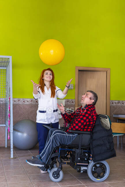 Jeune infirmière et homme handicapé jouant avec le ballon de fitness dans le centre de réadaptation — Photo de stock