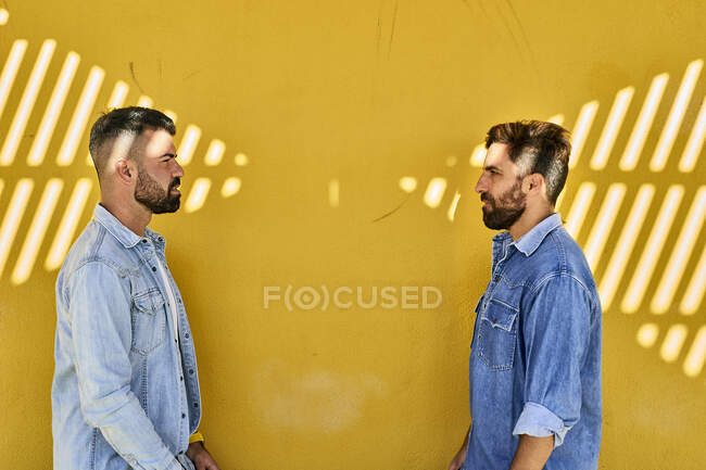 Gay casal olhando para cada outros enquanto pé contra amarelo parede — Fotografia de Stock