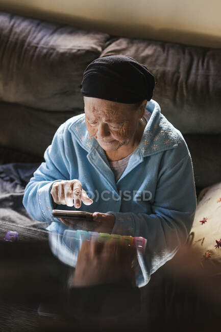 Пожилая женщина с мобильным телефоном в гостиной — стоковое фото