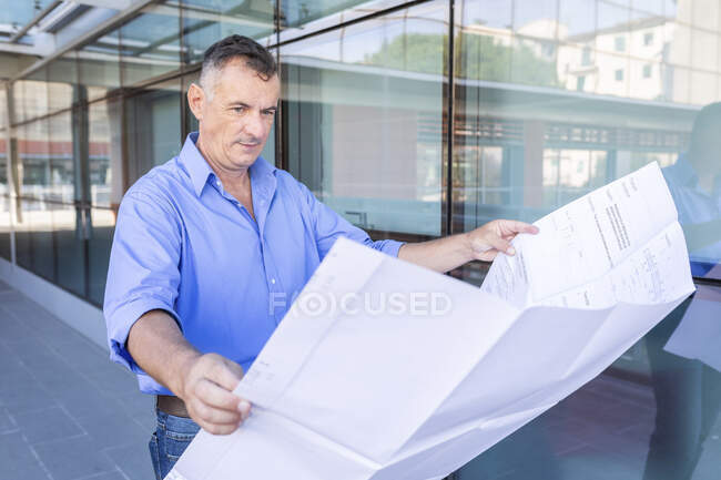 Empresario varón confiado mirando el plano del piso mientras que está parado en ciudad - foto de stock