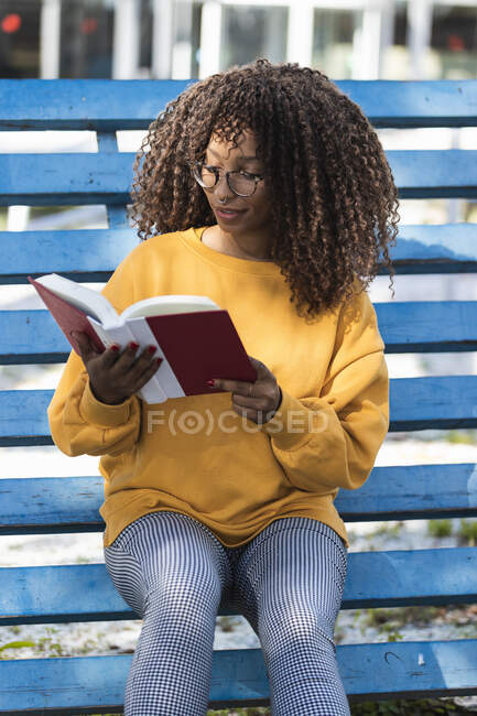 Модная молодая женщина читает книгу, сидя на голубых трибунах — стоковое фото