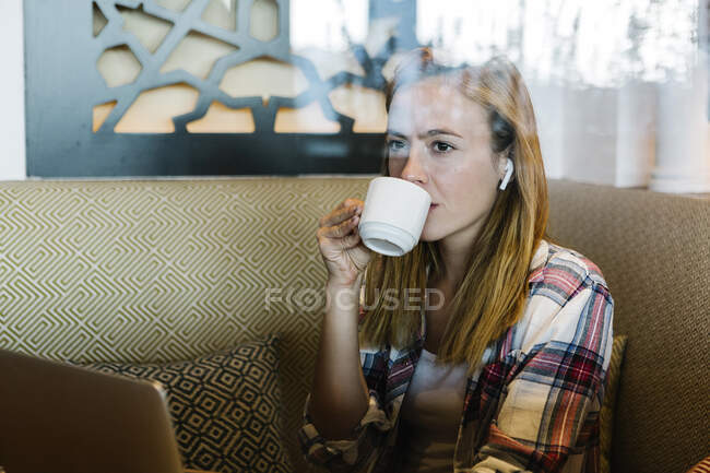 Mujer mirando hacia otro lado mientras bebe café sentado en casa - foto de stock