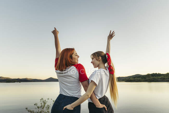 Carefree casal lésbico com as mãos nos bolsos de pé contra o céu limpo durante o pôr do sol — Fotografia de Stock