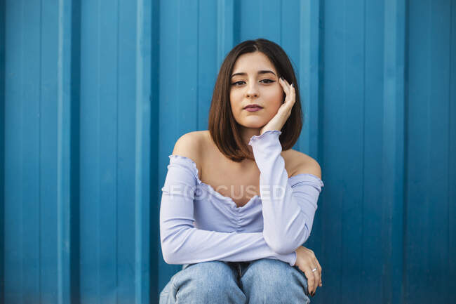 Молодая красивая женщина сидит у голубой стены — стоковое фото