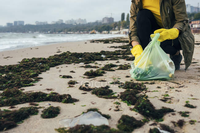Environmentalist collecting garbage in garbage bag while crouching at beach — Stock Photo
