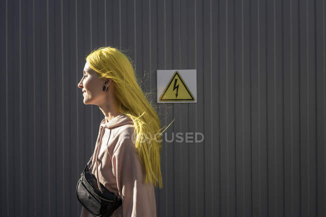 Jovem mulher olhando para longe, enquanto em pé por parede de metal no dia ensolarado — Fotografia de Stock