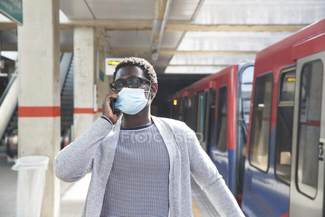 Empreendedor masculino usando máscara protetora ao falar no telefone celular na estação ferroviária — Fotografia de Stock