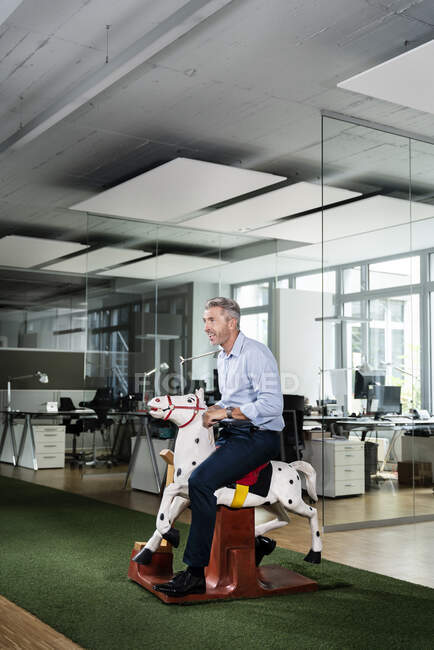 Бизнесмен смотрит в сторону, сидя на качающейся лошади в офисе — стоковое фото